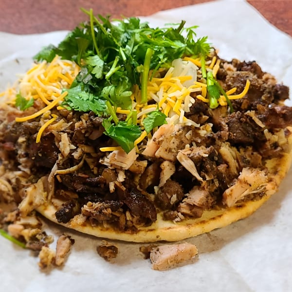 Jerk N Go's Jamaican flatbread topped with seasoned meat, shredded cheese, and fresh cilantro.