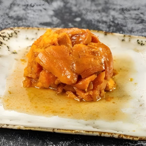 A serving of Jamaican candied yams, glistening with syrup, on a rustic white plate.