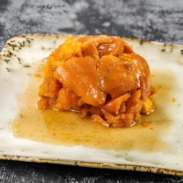A serving of Jerk N Go's candied yams, glistening with syrup on a rustic white plate.