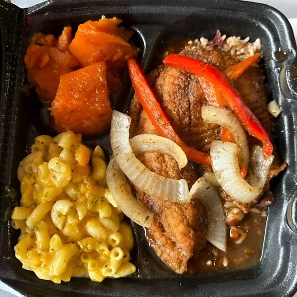 Jerk N Go's Jamaican meal with fried fish, mac and cheese, and candied yams in a takeout container.