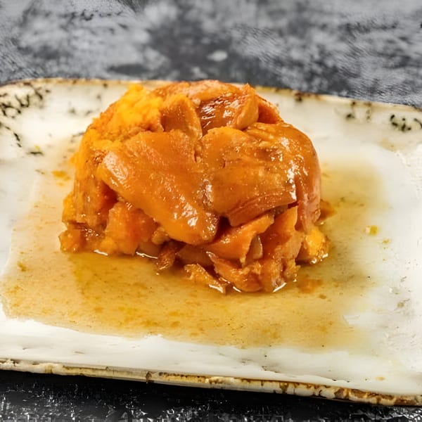 A serving of candied yams, glistening with syrup, on a rustic white plate.